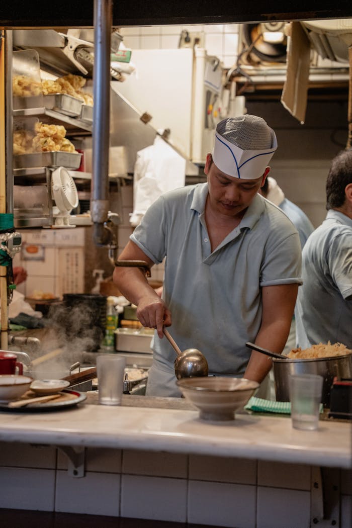 our-journey-01 A chef prepares food in a Shinjuku izakaya, Tokyo, showcasing traditional Japanese cuisine.