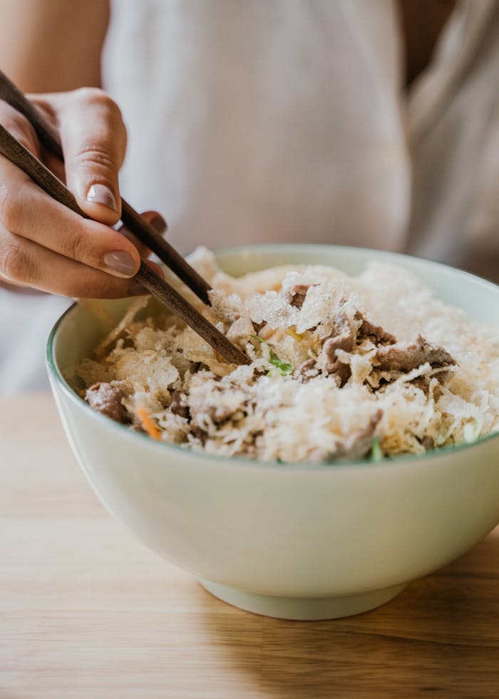 about-02 A hand using chopsticks to eat a delicious Asian dish in a bowl.