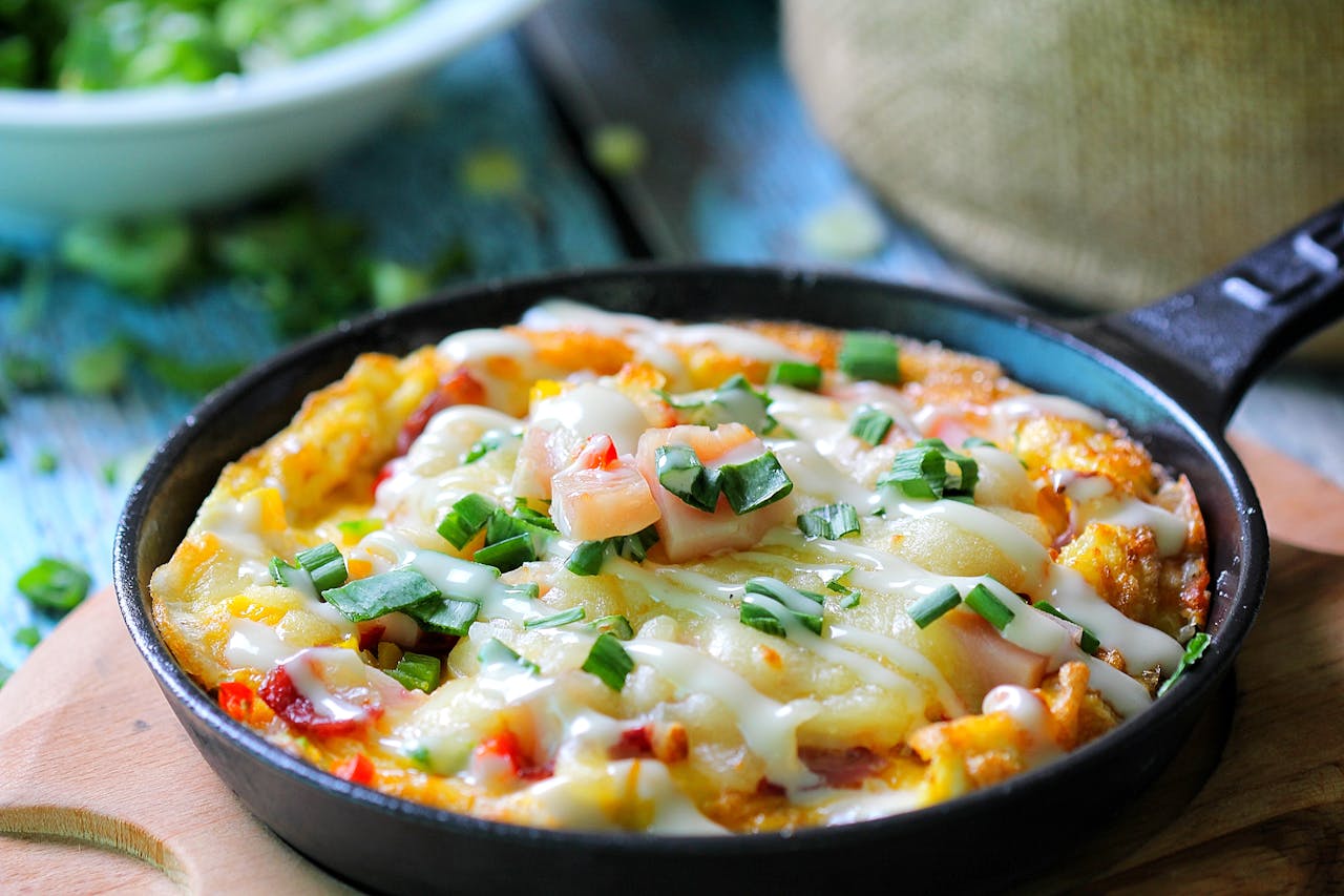 services-01 Close-up of a cheesy skillet dish topped with fresh herbs and green onions, perfect for food lovers.