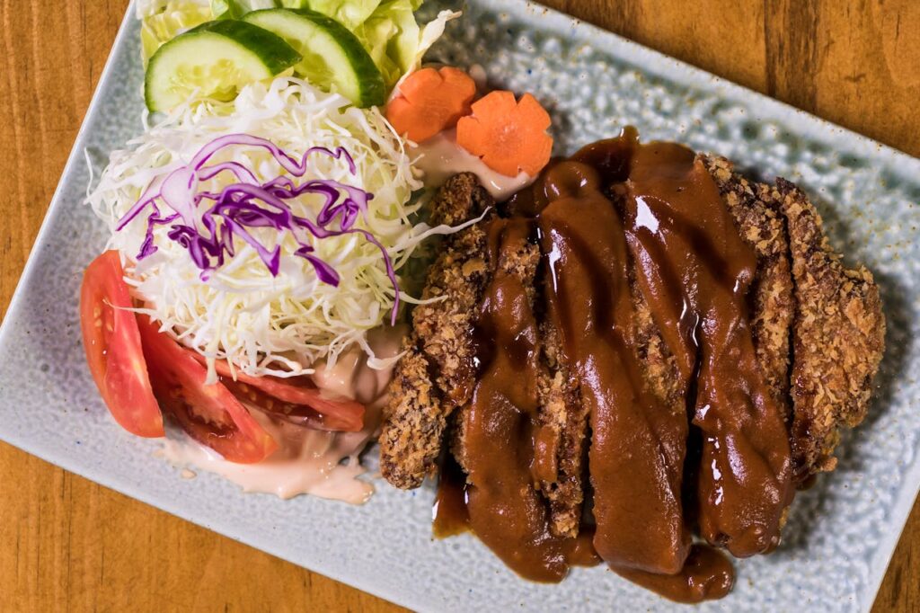 Crispy tonkatsu served with fresh vegetables and sauce, perfect for Japanese cuisine enthusiasts.